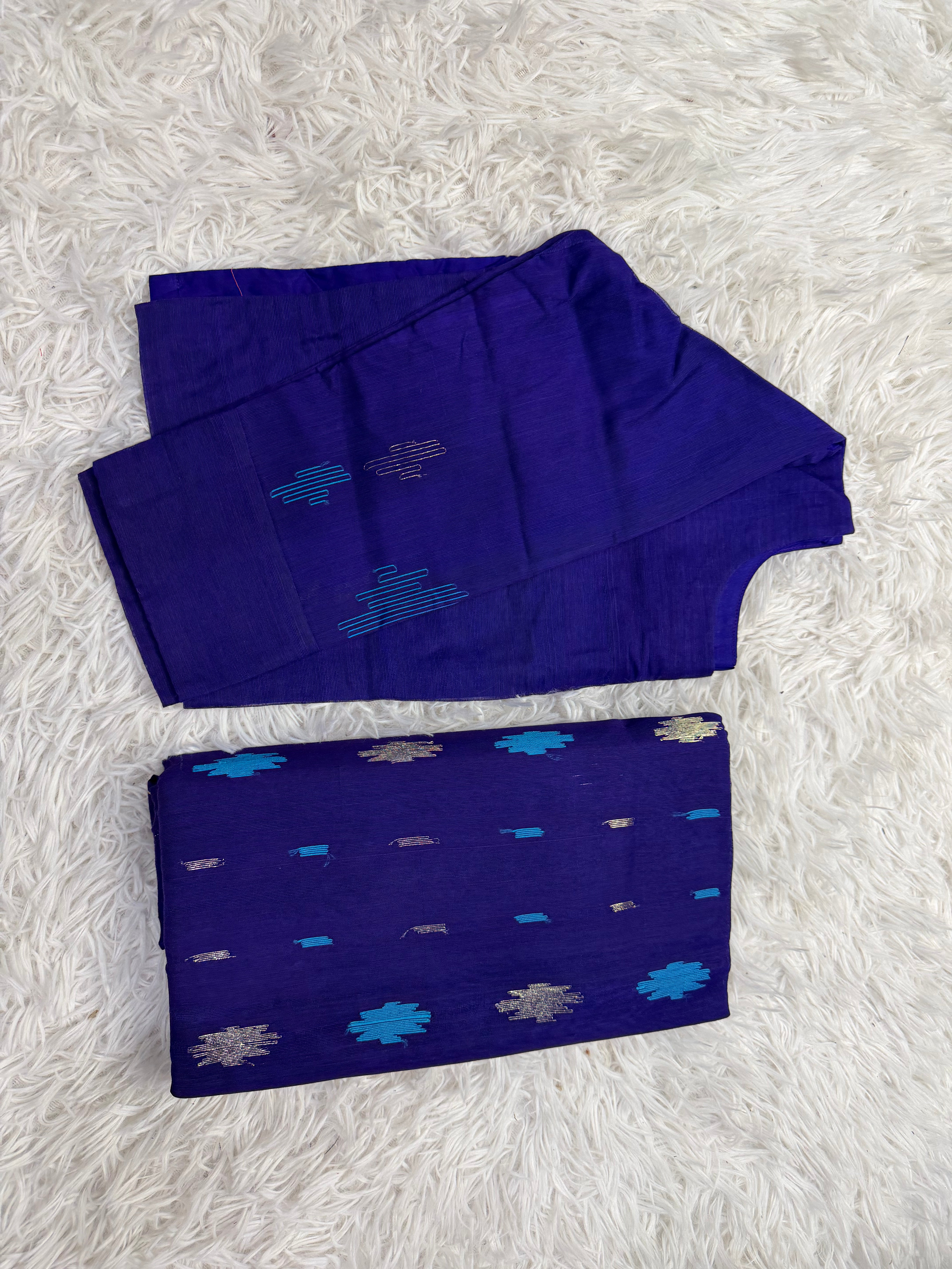 A folded royal blue fabric set, likely a traditional garment fabric or textile set, featuring blue and silver woven patterns, displayed on a white faux fur background.