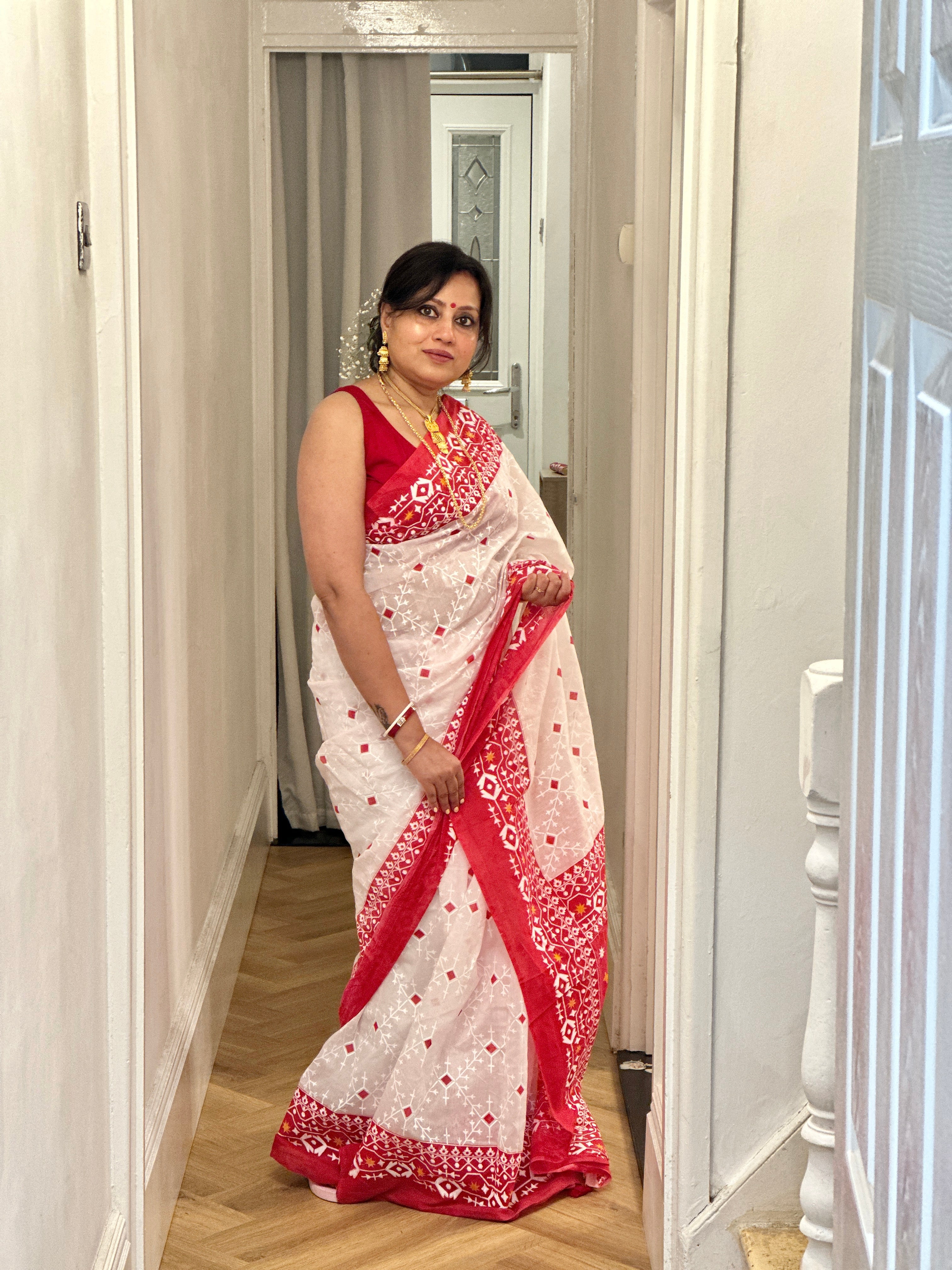 Woman wearing a red and white saree in a hallway.