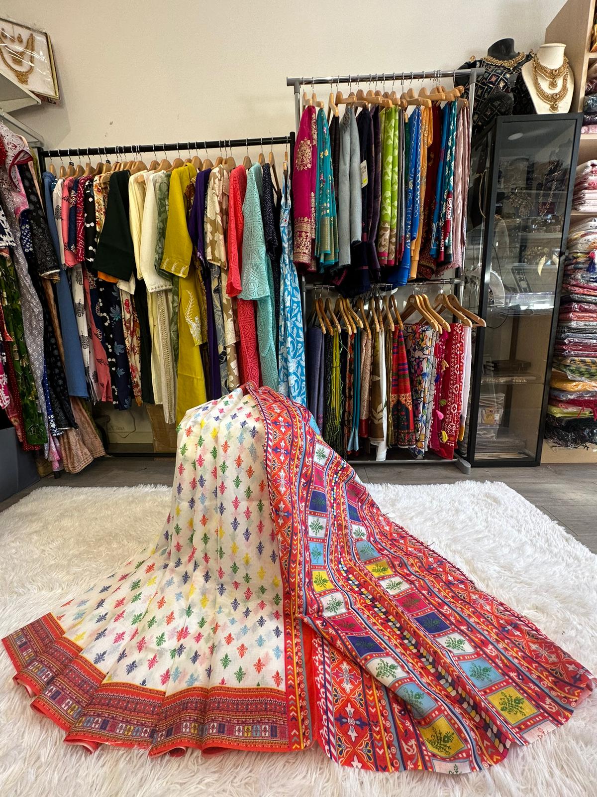 Colorful traditional fabric on a white rug with clothing racks in the background